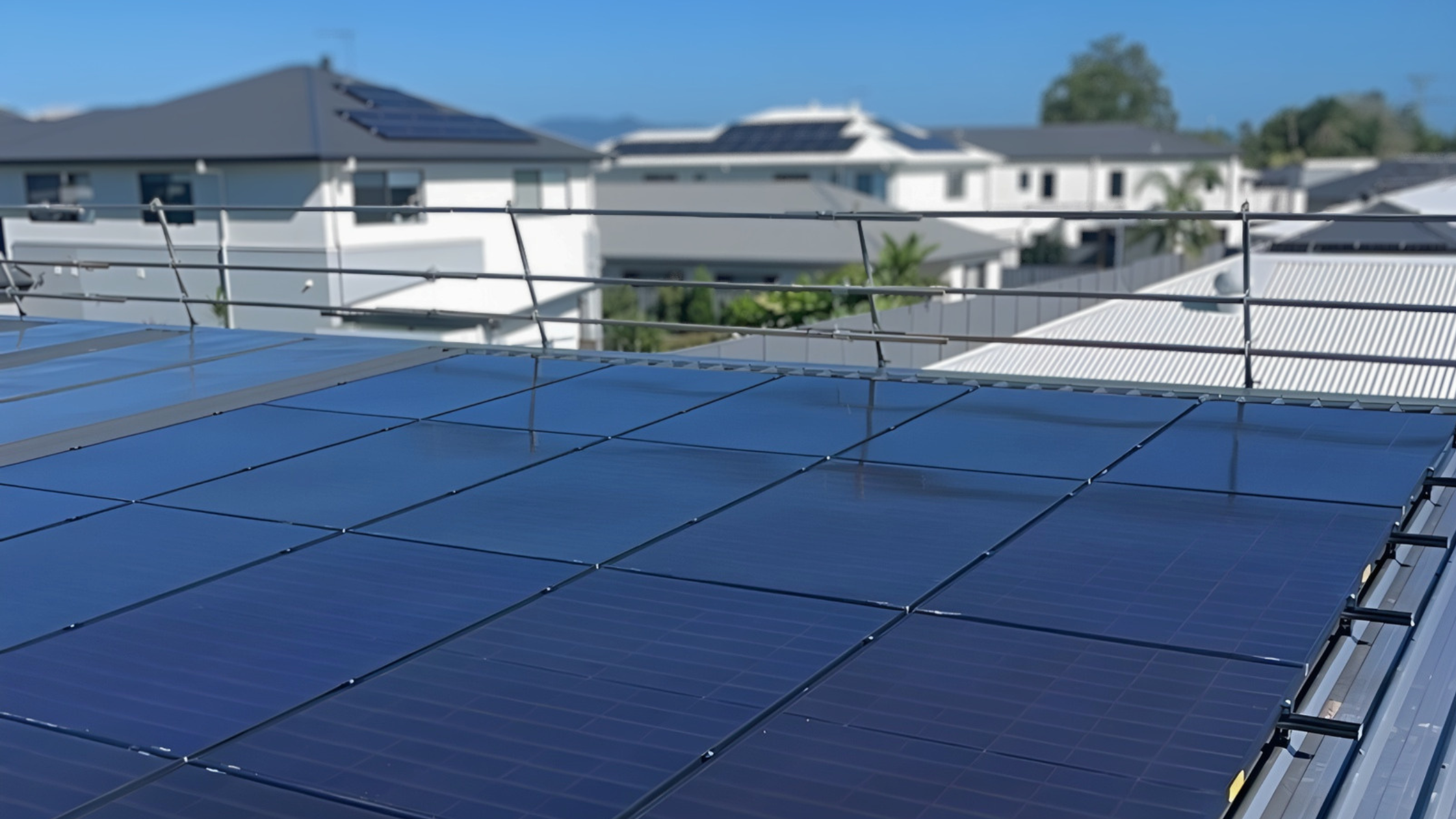 A rooftop with shiny solar panels under a clear blue sky, surrounded by modern suburban houses.