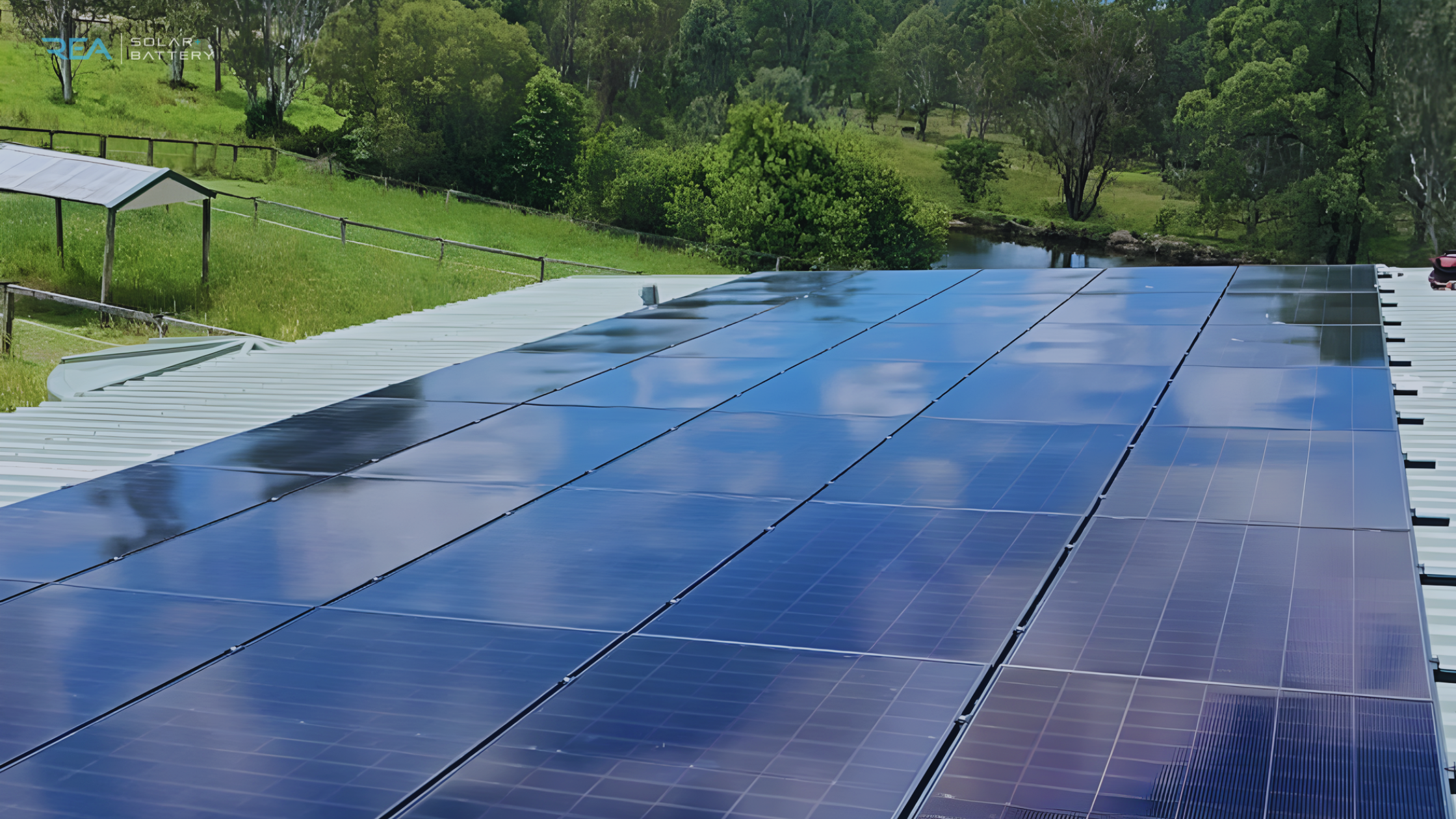 A rooftop with reflective solar panels under a cloudy sky, surrounded by lush greenery and a wooden fence, conveys a sense of sustainability and tranquility.