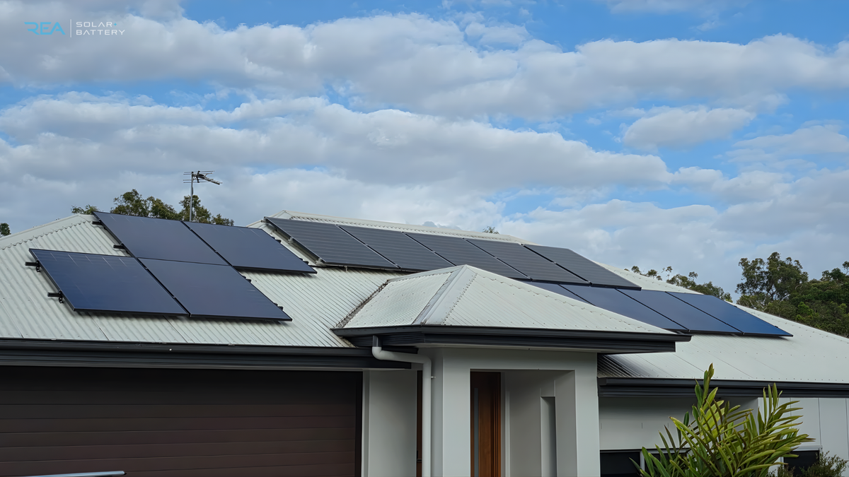 A house with a corrugated metal roof features several solar panels under a partly cloudy sky.